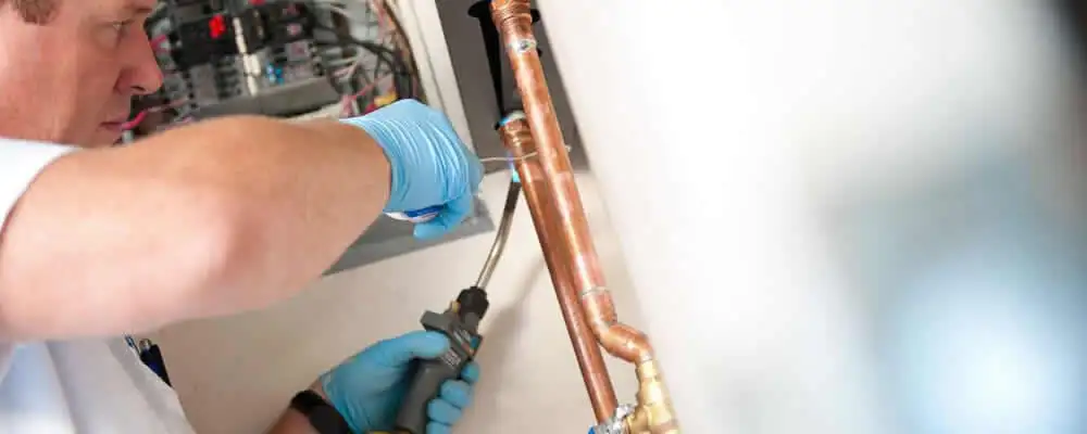 Water heater repair technician testing copper pipe connections and controls in Indianapolis, IN